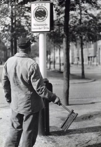 Figure 4: Traffic. Anti-noise campaign, man with cap and tool (rattle) in hand inspects a pole with KNAC sign stating that traffic discipline fosters silence. Place unknown (probably The Hague, 1935).